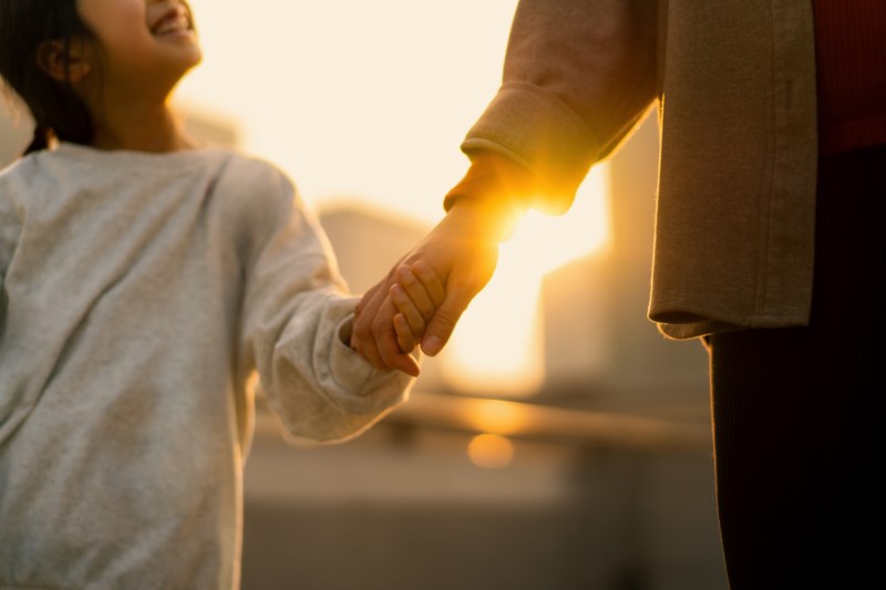 Barn og voksen holder hender i solnedgangen – et symbol på trygghet og tillit.