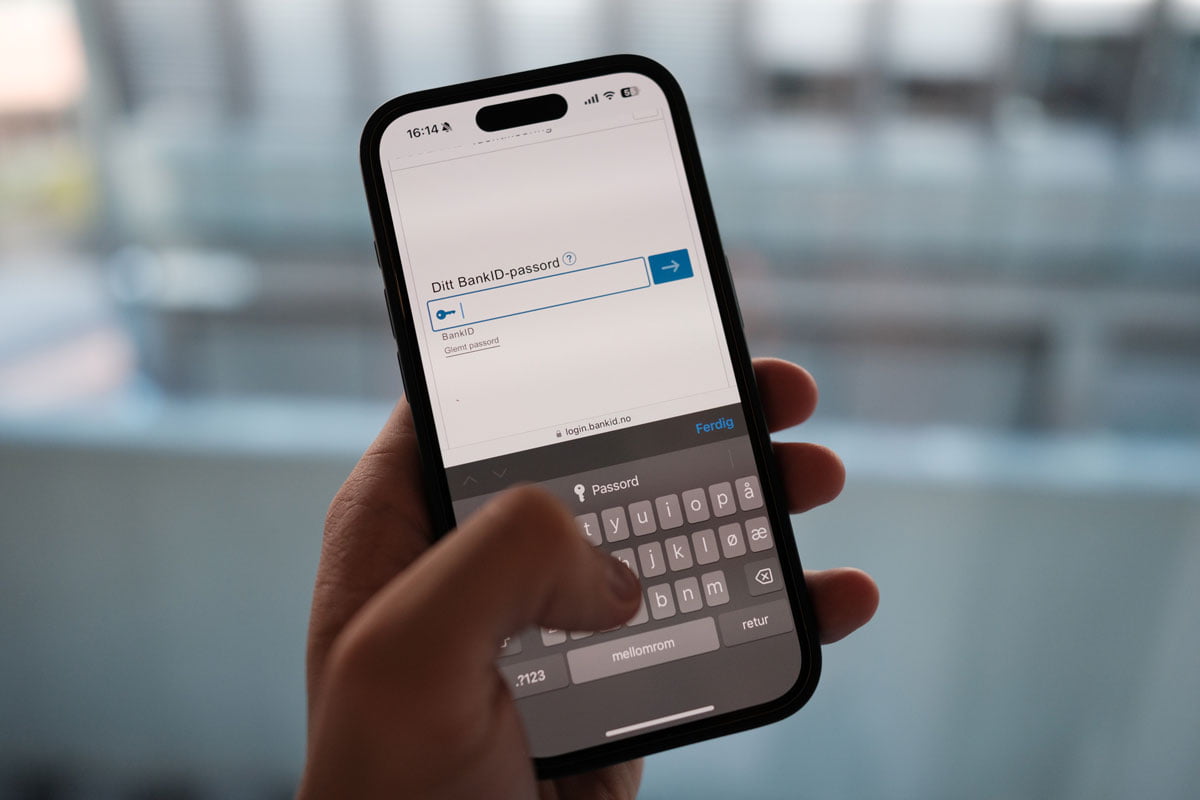 En person holder en mobiltelefon i hånden, klar til å skrive inn BankID-passordet på skjermen.